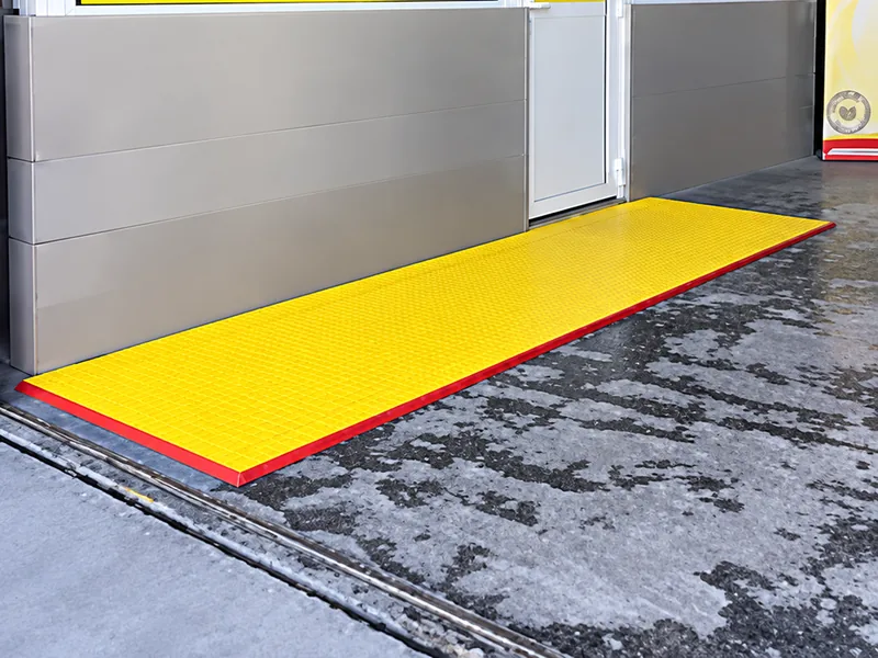 Alfombra de piso plástico amarilla con borde rojo en la entrada de un local