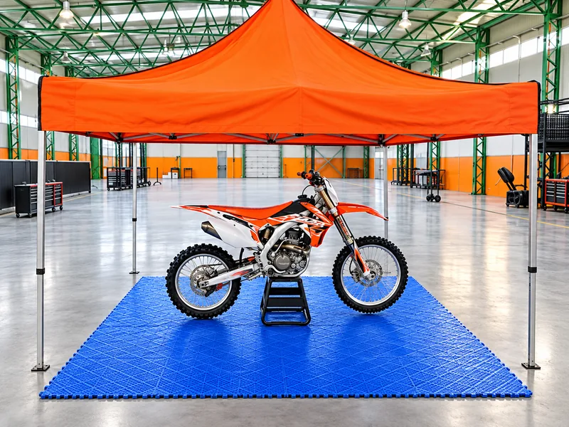 Moto de enduro exhibida sobre piso plástico azul bajo un gazebo naranja