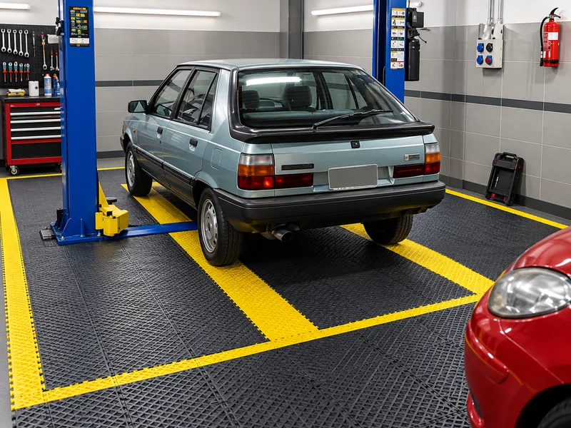 Taller mecánico con piso plástico negro y franjas amarillas bajo un elevador de autos
